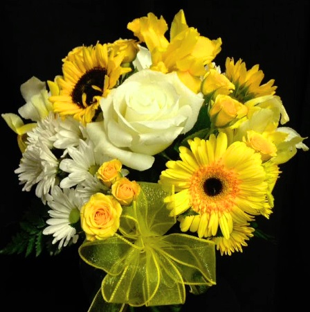 A floral arrangement with white and yellow roses, sunflowers, gerbera daisies, and white chrysanthemums tied with a yellow ribbon against a black background.