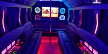 Interior of a party bus featuring purple and blue LED lighting, bench seating, and a dance floor.