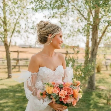 A bride with an elegant updo hairstyle holding a bouquet of flowers outdoors.