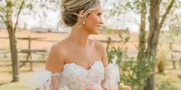 A bride with an elegant updo hairstyle holding a bouquet of flowers outdoors.