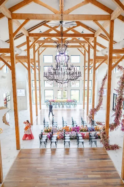Interior view of a wedding venue with high wooden beams, a large chandelier, and floral arrangements.