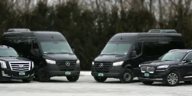 A lineup of four black luxury vehicles, including SUVs and limousines, parked on a paved surface.
