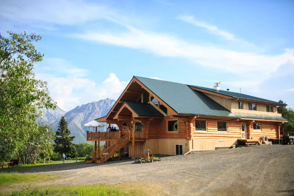 Exterior view of a large log cabin lodge with a mountain range in the background.