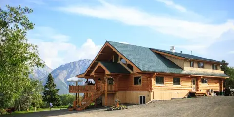 Exterior view of a large log cabin lodge with a mountain range in the background.