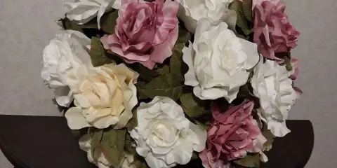 A floral arrangement of white and pink roses sitting on a dark wooden table.