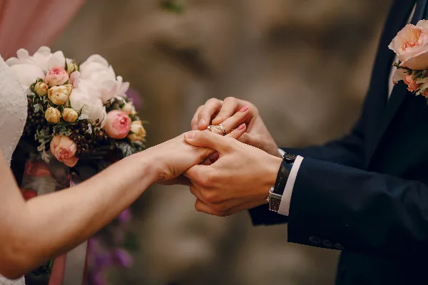 A groom placing a wedding ring on a bride's finger during a ceremony, with a floral bouquet in the foreground.