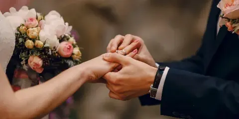 A groom placing a wedding ring on a bride's finger during a ceremony, with a floral bouquet in the foreground.