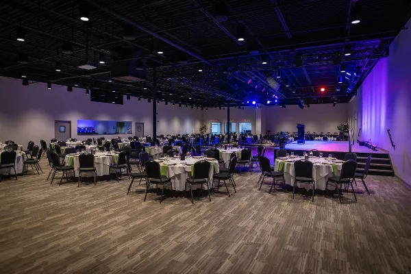 Interior view of a wedding reception hall with round tables, chairs, and a stage.