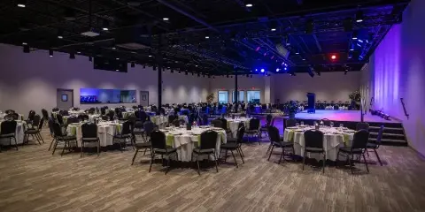 Interior view of a wedding reception hall with round tables, chairs, and a stage.