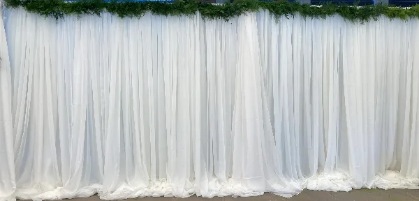 White fabric draping backdrop with greenery installed for an event