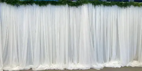 White fabric draping backdrop with greenery installed for an event