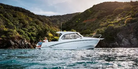 A white Beneteau Antares 8 motor yacht on calm water near a green hillside, with two people aboard, captured in a cinematic video still.