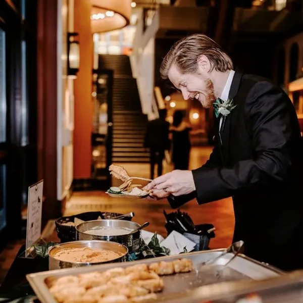 A catering server in a black suit plating food from a buffet station at an event.