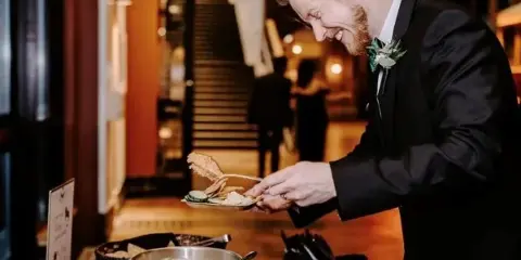 A catering server in a black suit plating food from a buffet station at an event.