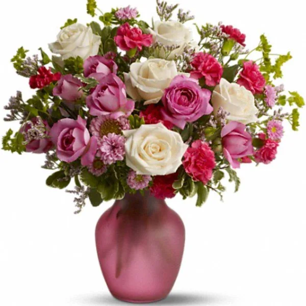 A floral arrangement of white and pink roses and carnations in a frosted pink vase.