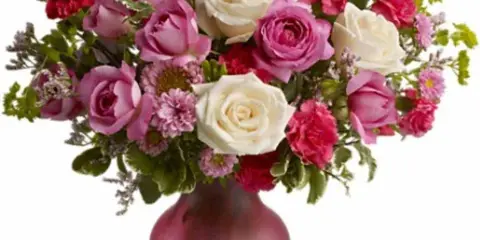 A floral arrangement of white and pink roses and carnations in a frosted pink vase.