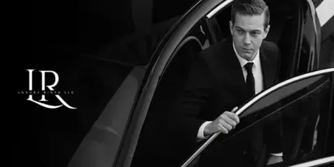 A professional chauffeur in a suit opening the door of a black luxury car.
