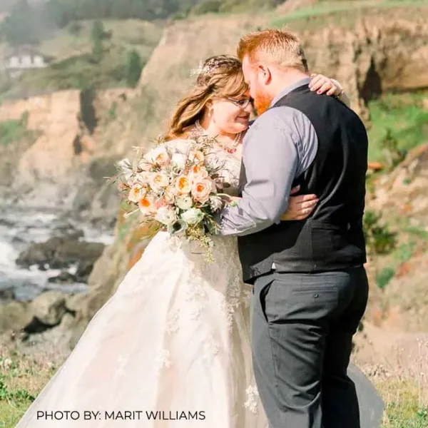 A bride and groom embracing on a coastal bluff with the ocean in the background.