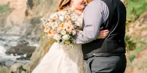 A bride and groom embracing on a coastal bluff with the ocean in the background.