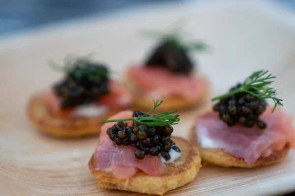 Plated appetizers with smoked salmon, cream cheese, caviar, and dill garnish on a wooden board