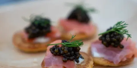 Plated appetizers with smoked salmon, cream cheese, caviar, and dill garnish on a wooden board