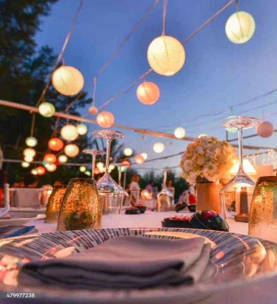 Elegant wedding reception table setting with floral centerpiece, glassware, and string lights.