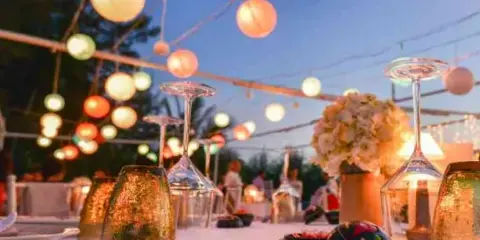 Elegant wedding reception table setting with floral centerpiece, glassware, and string lights.