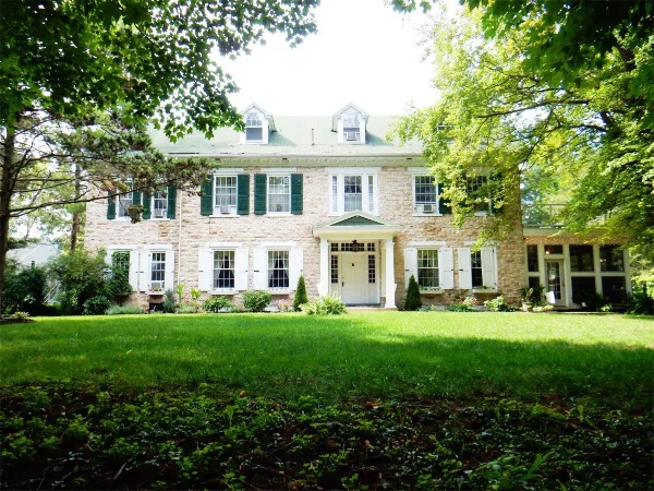 Exterior view of a large two-story stone building with green shutters and a manicured lawn, representing the Juniata Valley Winery estate.