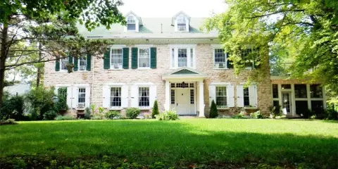 Exterior view of a large two-story stone building with green shutters and a manicured lawn, representing the Juniata Valley Winery estate.