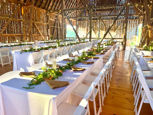 Interior of a rustic wooden barn set up for a wedding reception with long tables and white chairs.