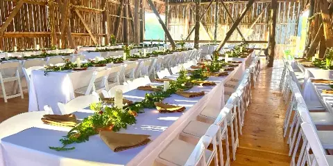 Interior of a rustic wooden barn set up for a wedding reception with long tables and white chairs.