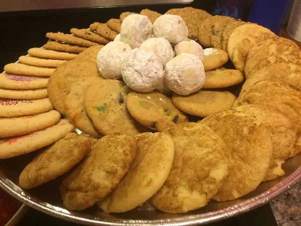 A large platter filled with various types of homemade cookies, including sugar cookies, chocolate chip cookies, and powdered snowballs.