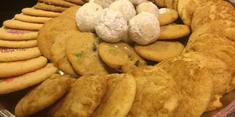 A large platter filled with various types of homemade cookies, including sugar cookies, chocolate chip cookies, and powdered snowballs.