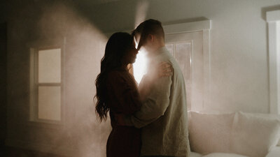 A cinematic still of a bride and groom embracing in a dimly lit room.