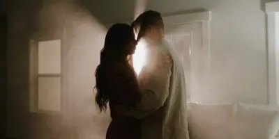 A cinematic still of a bride and groom embracing in a dimly lit room.