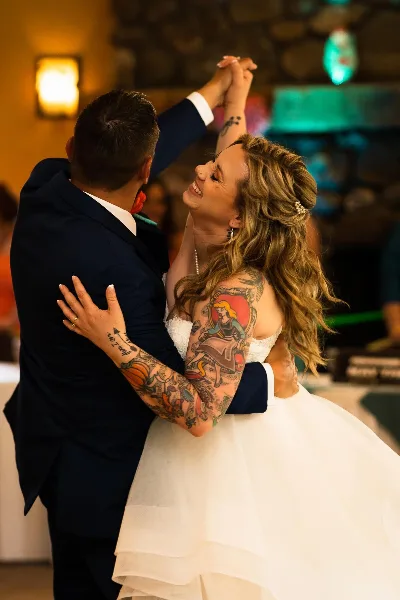 A bride and groom dancing together at a wedding reception, with the bride smiling and wearing a white dress and the groom in a dark suit.