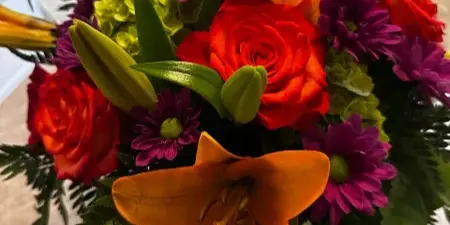 A vibrant floral arrangement featuring orange lilies, red roses, and purple chrysanthemums.