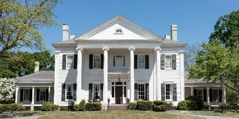 Exterior view of the white Bailey-Tebault House with columns and black shutters.