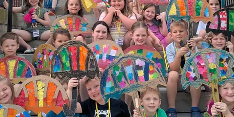 Children holding colorful fan-shaped art projects on the steps outside the Rowan County Arts Center