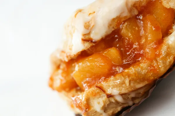 A close-up of a flaky pastry with a fruit filling and white glaze.