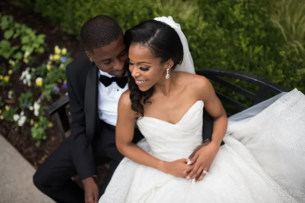A bride and groom sitting together on a bench in a garden setting.