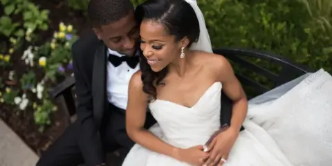 A bride and groom sitting together on a bench in a garden setting.