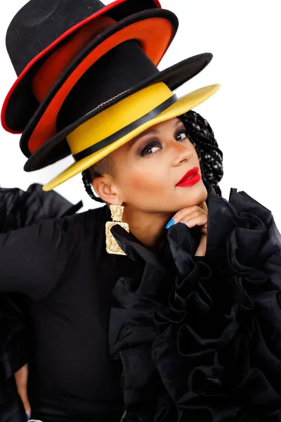 Portrait of DJ Valentina wearing a large, colorful stacked hat and black ruffled top.