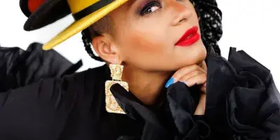 Portrait of DJ Valentina wearing a large, colorful stacked hat and black ruffled top.