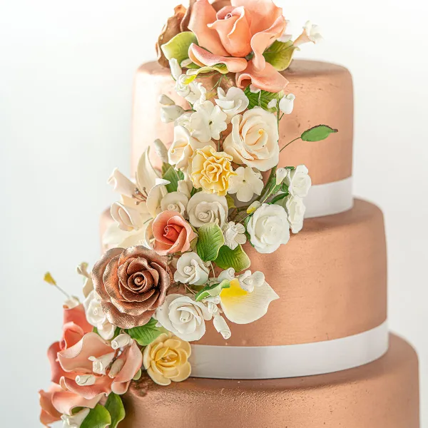 A three-tiered wedding cake with a metallic finish, decorated with cascading sugar roses and white flowers.