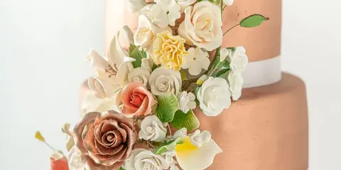 A three-tiered wedding cake with a metallic finish, decorated with cascading sugar roses and white flowers.
