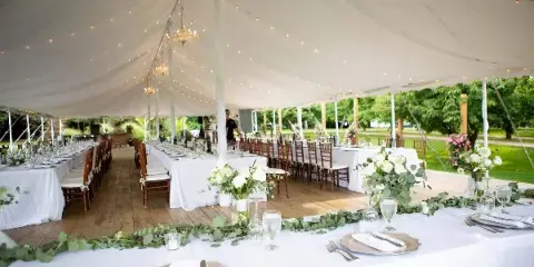 Interior view of a large white event tent set up for a wedding reception with long tables, chairs, and floral centerpieces.