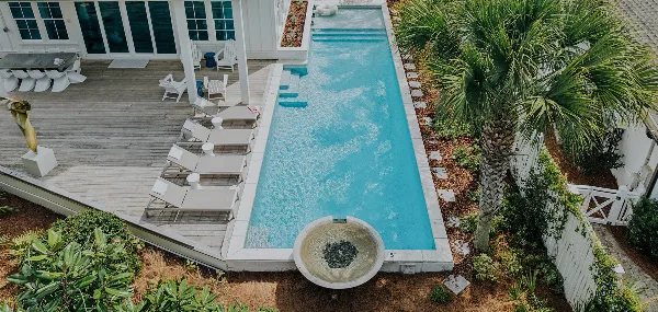 Aerial view of a luxury vacation home featuring a long swimming pool, wooden deck with lounge chairs, and palm trees.