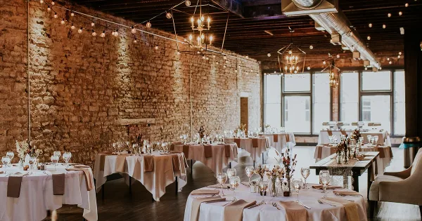 Interior of a restored event venue with exposed stone walls, string lights, and set dining tables.