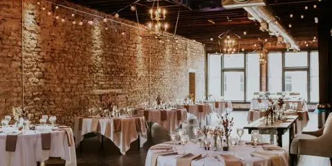 Interior of a restored event venue with exposed stone walls, string lights, and set dining tables.